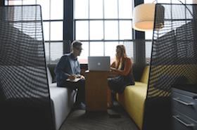 Two people sitting in a booth working on one computer